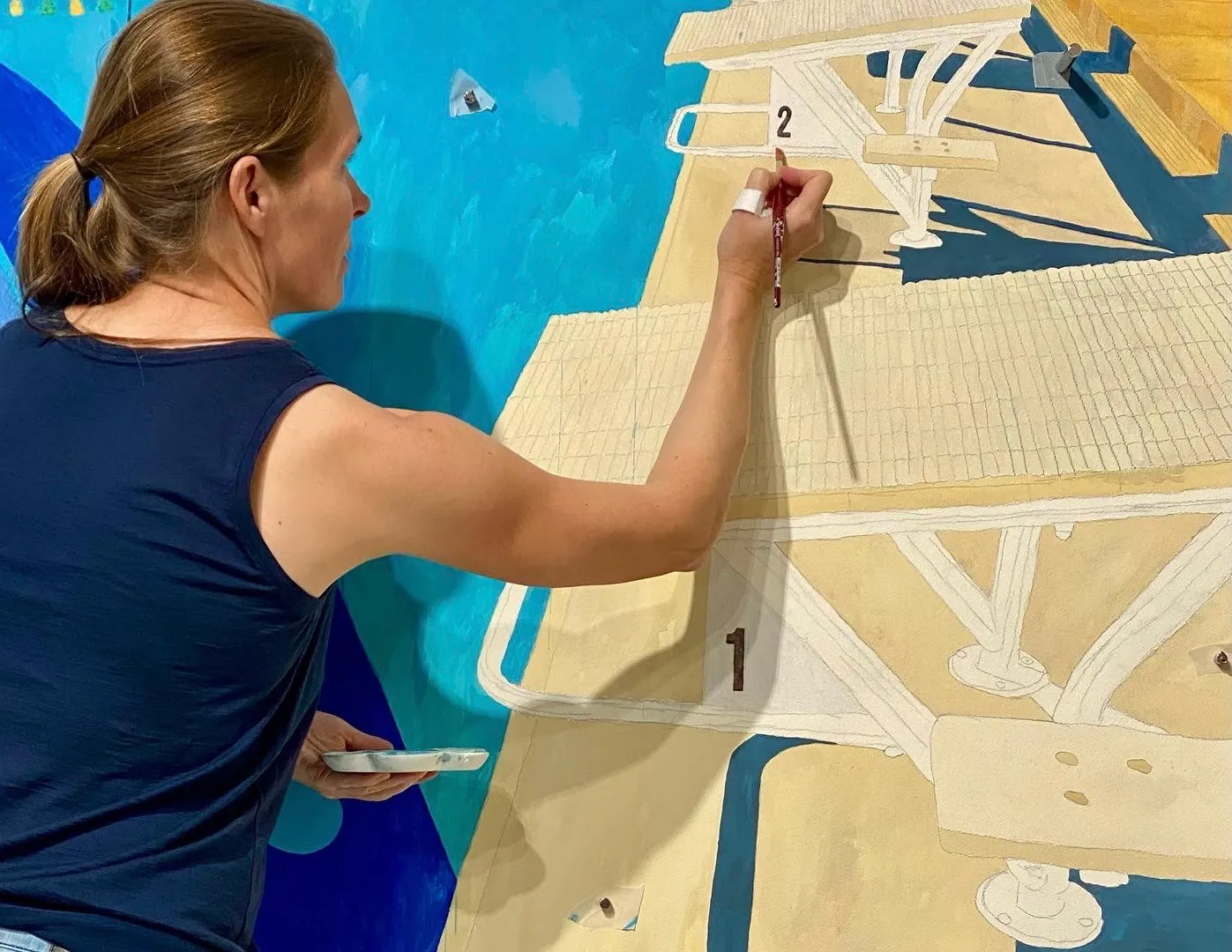 Henriette Dedichen painting a large-scale egg tempera work in her studio, seen from behind as she applies pigment to paper mounted on the wall